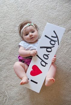 a baby holding a sign that says i love you on it's chest and sitting on the floor