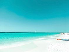 people are walking on the beach with their surfboards in the sand and clear blue water