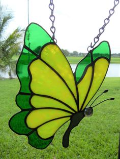 a stained glass butterfly hanging from a chain in the grass near a body of water