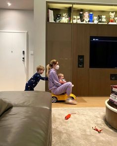 two children sitting on a toy car in front of a flat screen tv and bookshelf