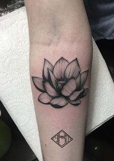 a black and white lotus flower tattoo on the right arm, with an initial letter b in the middle