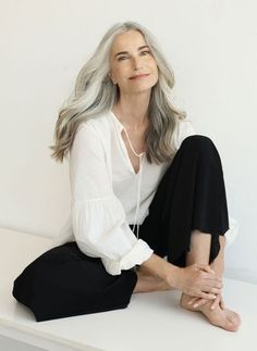 an older woman with grey hair sitting on a white bench wearing black pants and a white shirt