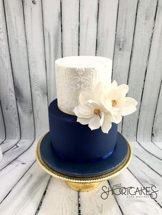 a blue and white wedding cake with two flowers on the top, sitting on a wooden table