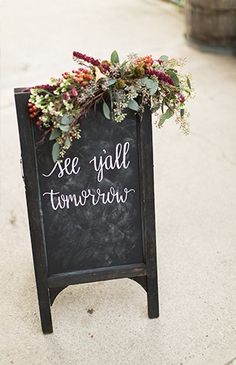 a chalkboard sign that says see y'all tomorrow with flowers and greenery