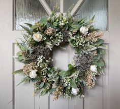 a wreath with flowers and greenery hanging on the front door to welcome guests into the house