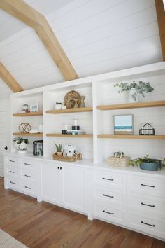 a room with white cabinets and wooden shelves filled with plants, vases and other items