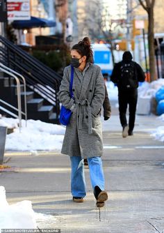 a woman walking down the street wearing a coat and talking on a cell phone while holding a blue bag