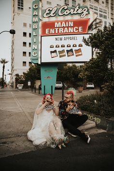 two people sitting on the ground in front of a sign with a building behind them