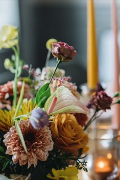 a vase filled with lots of different flowers on top of a table next to candles