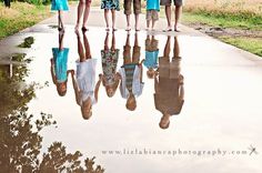 a group of people standing next to each other in front of a puddle with umbrellas