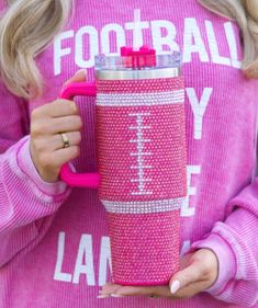 a woman holding a pink coffee cup with the word football on it in front of her