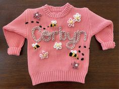 a pink sweater with flowers and the word sorry written on it is laying on a wooden surface