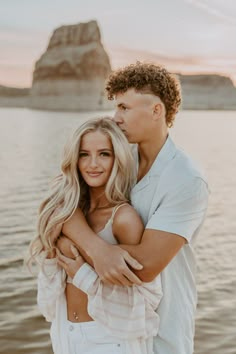 a man and woman standing next to each other in front of the water at sunset