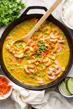 a skillet filled with shrimp, peas and carrots next to bowls of rice