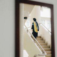 a person walking down some stairs with a scarf on their back and a mirror reflecting them