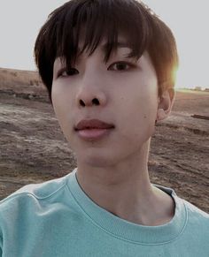 a young man standing in front of a dirt field with the sun shining on him