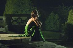 a woman in a green dress is sitting on some steps and looking off into the distance