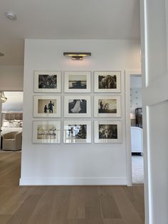 a wall with many pictures hanging on it's side in a room that has hardwood floors and white walls