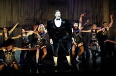 a man in a tuxedo is surrounded by dancers