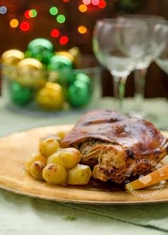 a piece of meat and potatoes on a plate next to some wine glasses with christmas lights in the background