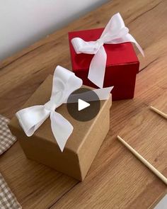 two small boxes with white bows on them sitting on a table next to knitting needles