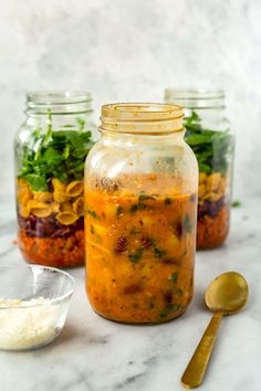 three mason jars filled with food on top of a white marble counter next to spoons