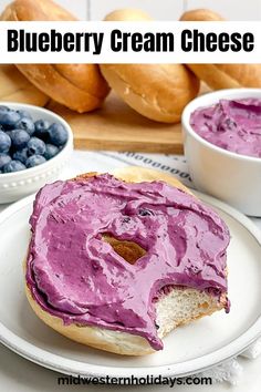 a blueberry cream cheese sandwich on a white plate with berries and bagels in the background