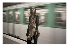 a woman standing in front of a train with her hand on her hip and looking at the camera