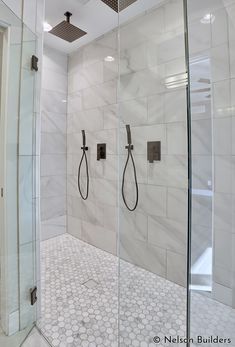 a walk in shower sitting next to a white tiled wall and floor with two black hand held shower heads