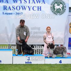 two people standing on a podium with their dogs at a dog show in front of a banner