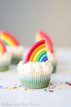 cupcakes with rainbow decorations and ribbons on a marble countertop in front of confetti