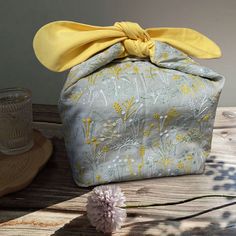 a yellow bow sits on top of a gray and white bag next to a pink flower