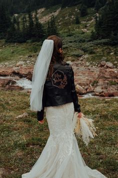 the back of a bride's jacket and wedding dress in front of a mountain stream