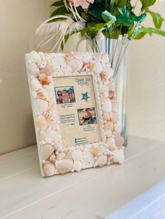 a vase filled with flowers and shells on top of a white shelf next to a framed photo