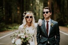 a man and woman standing next to each other in front of a road with trees