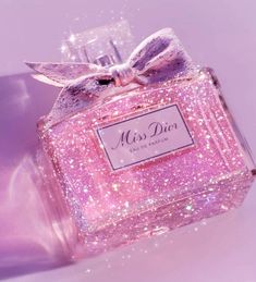 a pink perfume bottle with a bow on it's top and sparkles in the background