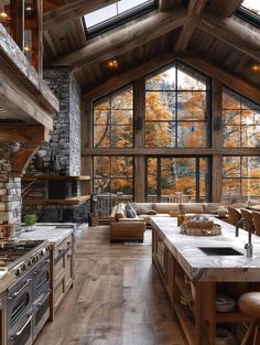 an open kitchen and living room area with wood flooring, stone fireplaces, and large windows