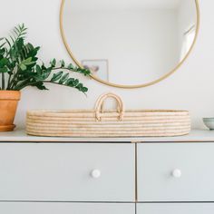 a basket sitting on top of a dresser next to a mirror and potted plant