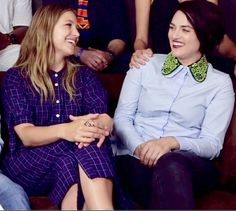 two women sitting next to each other in front of a group of people wearing collared shirts