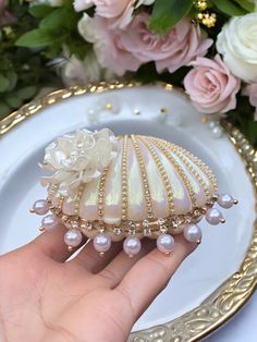 a hand holding a seashell with pearls and flowers in the background on a plate