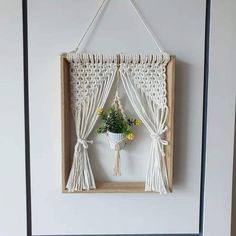 a white wall hanging with flowers in a vase on it and some string attached to the frame