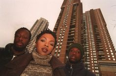 two men and a woman standing in front of a tall building with skyscrapers behind them