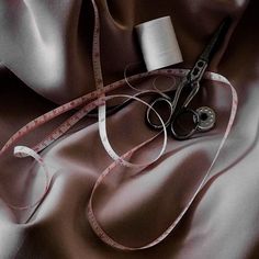 a pair of scissors sitting on top of a brown satin covered table cloth next to a measuring tape