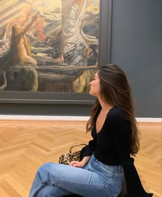 a woman sitting on the floor in front of a painting looking up at her purse