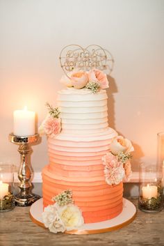 a three tiered cake with flowers on top and candles around the edges, sitting on a wooden table