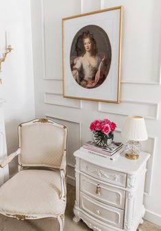 a white chair sitting in front of a painting on the wall next to a dresser