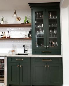 a kitchen with green cabinets and marble counter tops, wine glasses on the glass doors