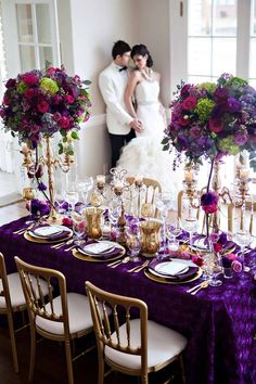 a bride and groom standing next to each other in front of a table with purple flowers