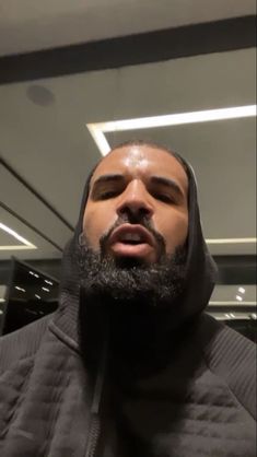 a man with a beard wearing a hoodie and looking up at the ceiling in front of him