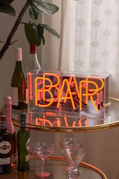 an illuminated bar sign sitting on top of a glass table next to bottles and glasses